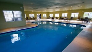 An indoor swimming pool with a curved design, surrounded by lounge chairs and tables. - Branson | Family Lake Retreat | Pool + Lake | 2BR (Branson)