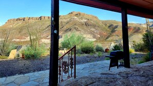 Um espaço ao ar livre coberto com um pátio de pedra, guarda-corpo de metal e vista para uma paisagem montanhosa.