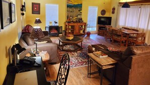 Uma sala de estar acolhedora com lareira, televisão, espaço de jantar e ventilador de teto.