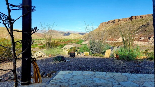 Uma área externa coberta com piso de pedra, vegetação de desert e vista para montanhas ao longe.
