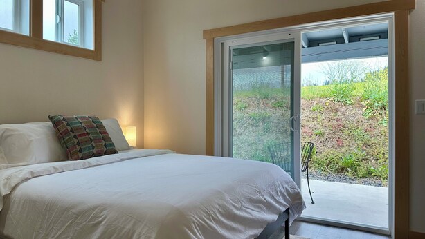 Un dormitorio con cama, ventana y puerta corredera de vidrio que da a un espacio exterior.