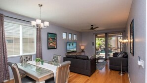 A modern living room with a glass dining table, dark sofas, and a ceiling fan. - Poolside Paradise Terramar Family Safe Retreat Beautiful Northwest Peoria (Peoria)
