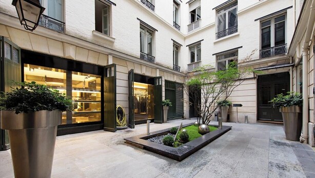 Un pati amb un edifici modern, grans jardineres i una petita zona verda.