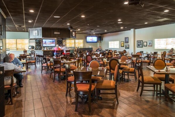 Un restaurante con varias mesas y sillas, una zona de bar con televisor y una barra.