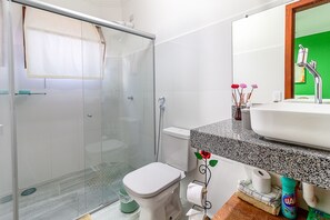 A bathroom with a glass shower enclosure, a white toilet, a sink with a granite countertop, and a mirror with a green accent wall. - Sítio de Praia (Porto Seguro)