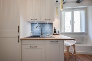 A modern kitchen with white cabinets, a blue-tiled backsplash, a stainless steel sink, and a window with a view of the outside.
