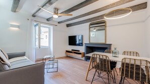 Een moderne woonkamer met een bank, eettafel, rieten stoelen, een televisie en een open haard.