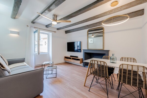 A modern living room with a sofa, dining table, wicker chairs, a TV, and a fireplace.