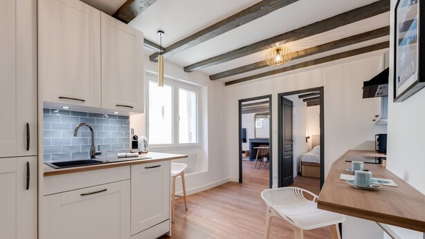 Een moderne keuken met witte kasten, een zwarte spoelbak en een houten aanrecht. Er is een raam dat natuurlijk licht binnenlaat, en een houten plafond met zichtbare balken.