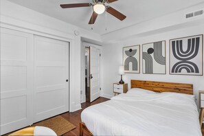 Un dormitorio con cama de madera, paredes blancas y una obra de arte abstracta.