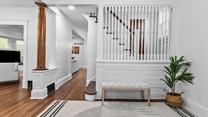 A spacious living area with hardwood flooring, a white bench, and a staircase with white railings.