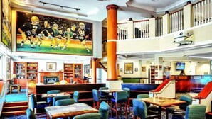 A hotel lobby with a large sports-themed mural, multiple seating areas, a fireplace, and a staircase to an upper level.