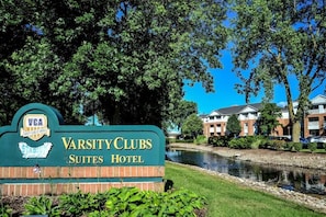 A sign for Varsity Clubs Suites Hotel with a clear view of the surrounding buildings and a body of water.