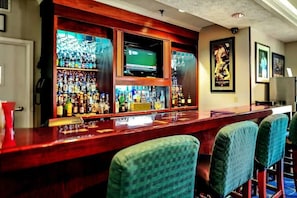 A bar area with a television, shelves of liquor bottles, and bar stools.