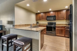 A compact kitchen with a granite countertop, stainless steel appliances, and wooden cabinets.