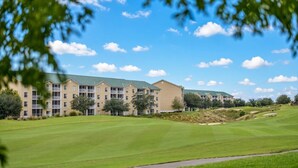 A multi-story hotel with a green lawn in front, surrounded by trees and a clear sky.