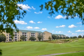 A multi-story hotel with a green lawn in front, surrounded by trees and a clear sky.
