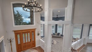 A spacious living area with a large window, a chandelier, and a wooden door. - Rosie's Retreat (Cornelius)