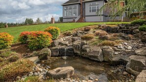 A house with a pond, surrounded by a landscaped garden with rocks and shrubs. - Rosie's Retreat (Cornelius)