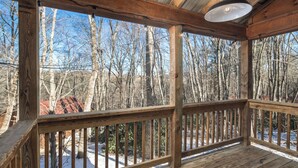 A wooden deck with a metal roof, overlooking a snowy landscape with bare trees.