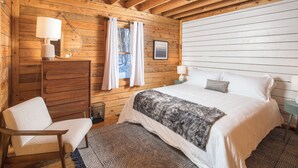 A cozy wooden cabin bedroom with a bed, a chair, a dresser, and a ceiling fan.