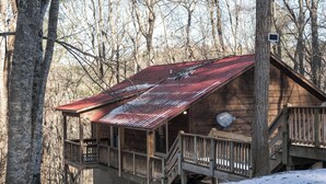 A wooden cabin with a metal roof, a balcony, and a staircase leading to the upper level.