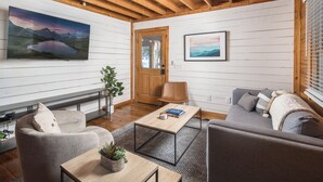 A modern living room with a wooden ceiling, a flat-screen TV, a sofa, a coffee table, and a door.