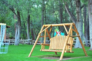 A wooden swing set in a park with green grass and trees. - Payson | Efficient Cabin Stay | Pool + Hot Tub (Payson)
