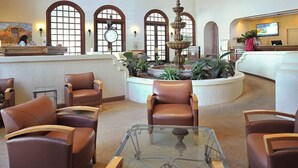 A lobby with leather chairs, a glass coffee table, a fountain, and arched windows.