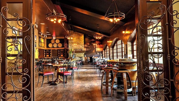 A spacious restaurant with high ceilings, exposed brick walls, and large windows.