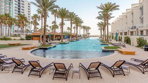 A pool area with lounge chairs, palm trees, and a building with multiple floors. - Beachfront Vacation Condo at the Sapphire (South Padre Island)