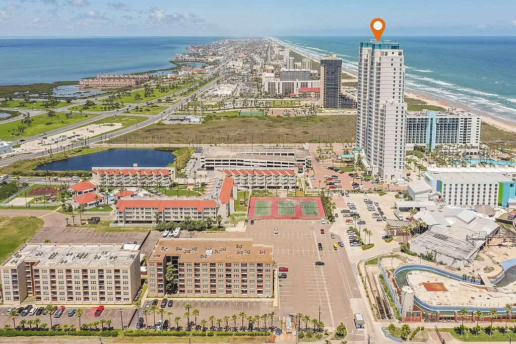 Um hotel alto com vista para o oceano, um estacionamento e um campo esportivo.