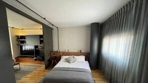 Ein modernes Hotelzimmer mit einem großen Bett, Holzboden, Fernseher und einer Schiebetür.