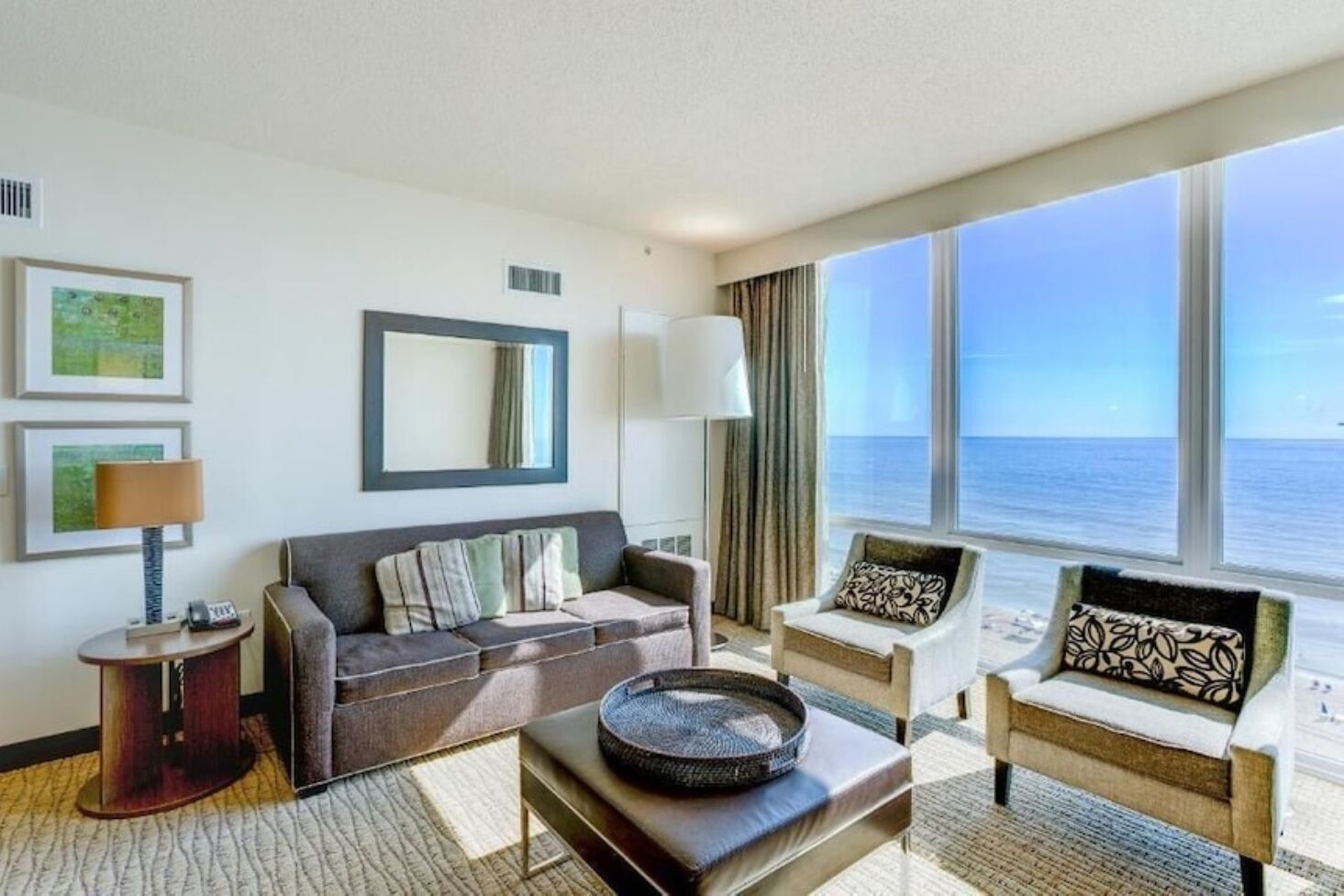 A hotel room with a sofa, armchair, and a view of the ocean.
