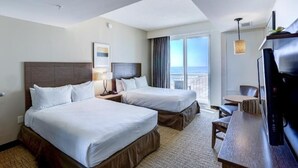 Camera d'albergo con due letti, una scrivania, una sedia, una TV e un'ampia finestra vista spiaggia.