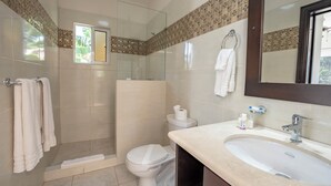 Un baño moderno con ducha de vidrio, inodoro, lavamanos y espejo.
