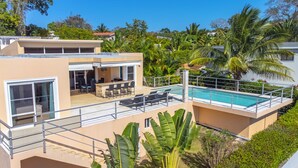 Una casa moderna con piscina, mobiliario de exterior y abundante vegetación.