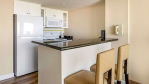 A compact kitchen with white cabinets, a microwave, a stove, and a small island with chairs.