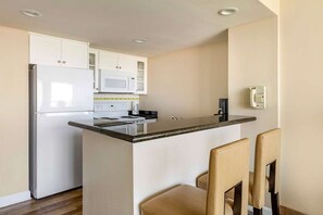 A compact kitchen with white cabinets, a microwave, a stove, and a small island with chairs. - Diamond Resorts Ocean Beach Club - 1 Bedroom Accessible No Roll-in Shower Ocean View (Virginia Beach)