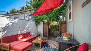 A cozy outdoor seating area with a red sofa, a wooden table, and a wicker chair, featuring a patterned rug and a red canopy. - Cozy historic downtown CDA home w/ office space. Pet friendly!  (Coeur d'Alene)