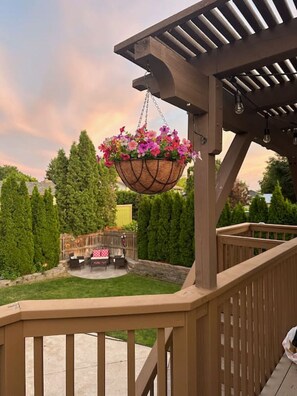A wooden deck with a hanging flower basket, a covered patio area, and a well-maintained lawn. - Playtime Paradise! Pool, Video Game Room, Pets OK! (Kennewick)