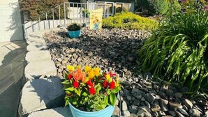 A modern two-story house with a stone pathway leading to the entrance, surrounded by a well-maintained garden with colorful flowers and shrubs. - Playtime Paradise! Pool, Video Game Room, Pets OK! (Kennewick)