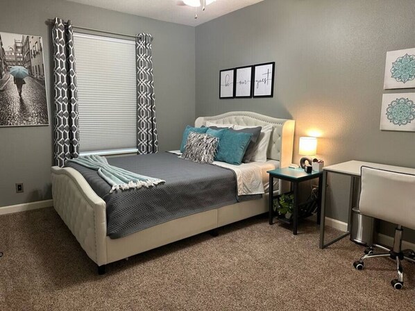 A bedroom with a bed, bedside table, lamp, and wall art. - Playtime Paradise! Pool, Video Game Room, Pets OK! (Kennewick)