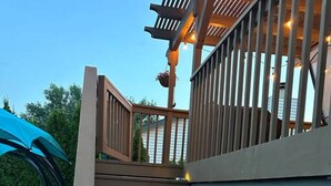 A wooden staircase with steps leading up to a covered area, a blue chair, and a railing with lights. - Playtime Paradise! Pool, Video Game Room, Pets OK! (Kennewick)