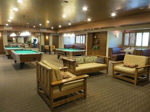 Une table de billard, des fauteuils confortables et une autre table de billard se trouvent dans une pièce bien éclairée, dont le sol est recouvert d’une moquette.