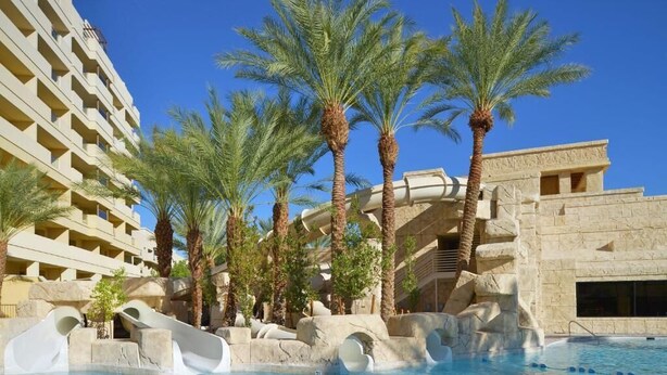 A hotel pool area with palm trees, a water slide, and a stone building.