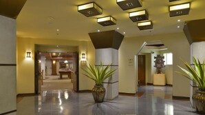 A spacious lobby with a polished floor, potted plants, and modern lighting fixtures.