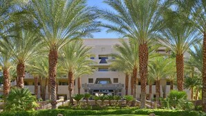 A hotel with a symmetrical facade, palm trees, and a well-maintained lawn.