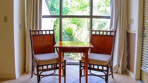 Una habitación con un gran ventanal, dos sillas de madera, una mesita y cortinas.