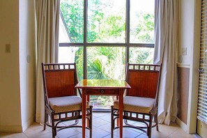 Ein Zimmer mit großem Fenster, zwei Holzstühlen, einem kleinen Tisch und Vorhängen.